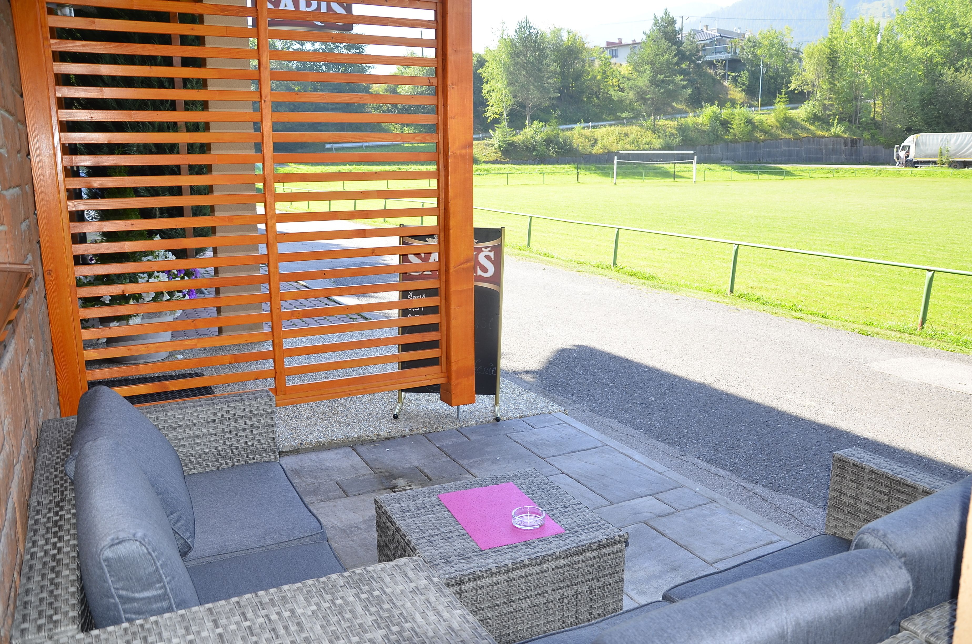 Een terras met rieten meubilair, een roze placemat en uitzicht op een sportveld.