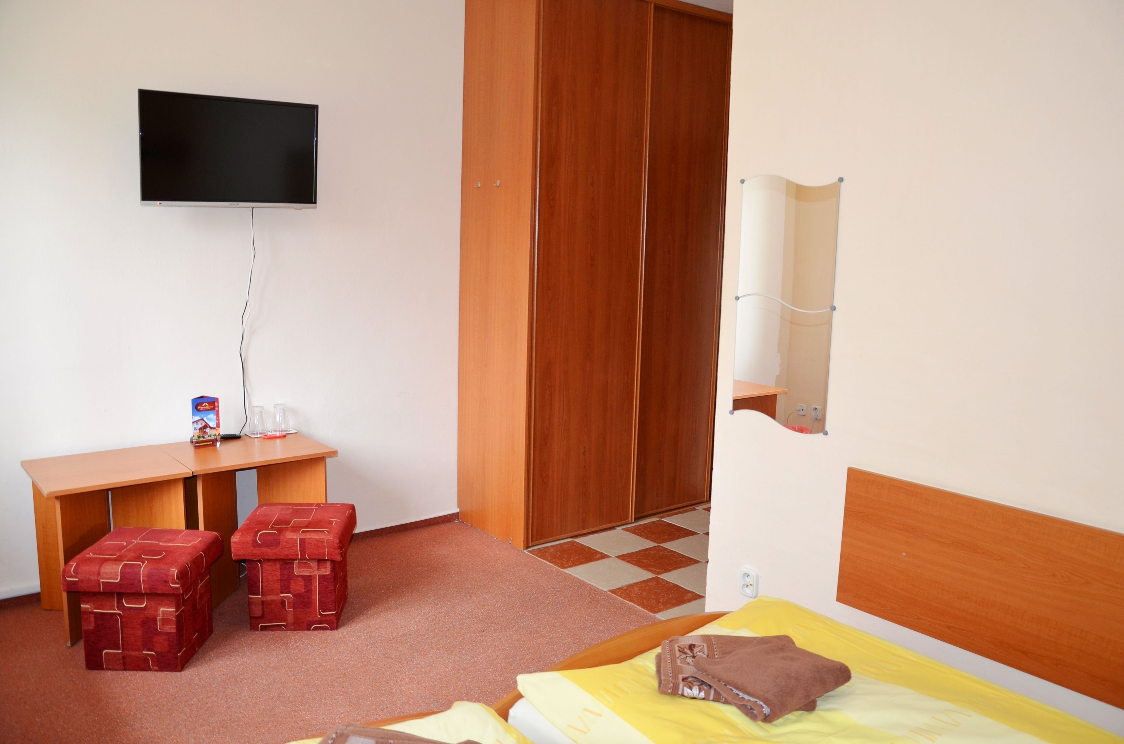 Una habitación con una cama, un escritorio con una silla, un televisor en la pared y un armario.