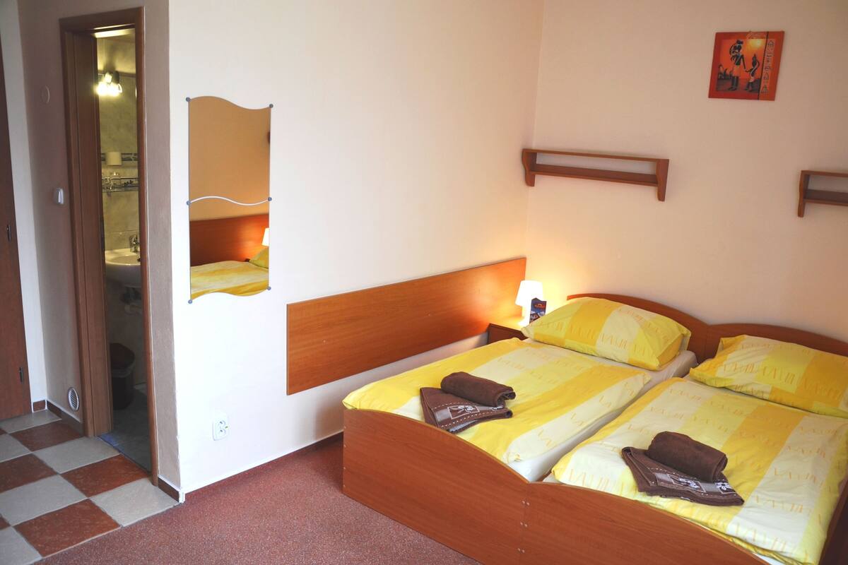 A double bed with yellow and white bedding, a wooden headboard, and a bedside table with a lamp.
