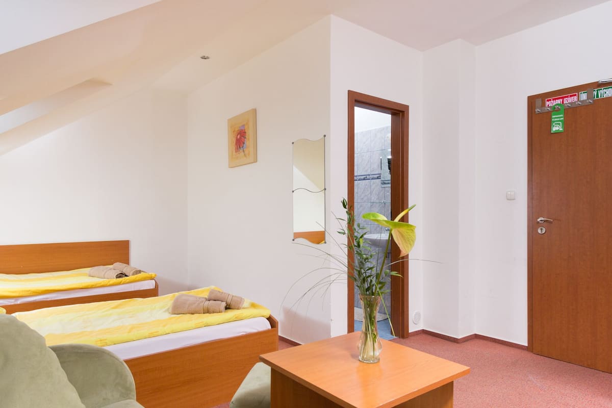 A hotel room with two beds, a wooden desk, a vase with flowers, a mirror, and a door with signs.