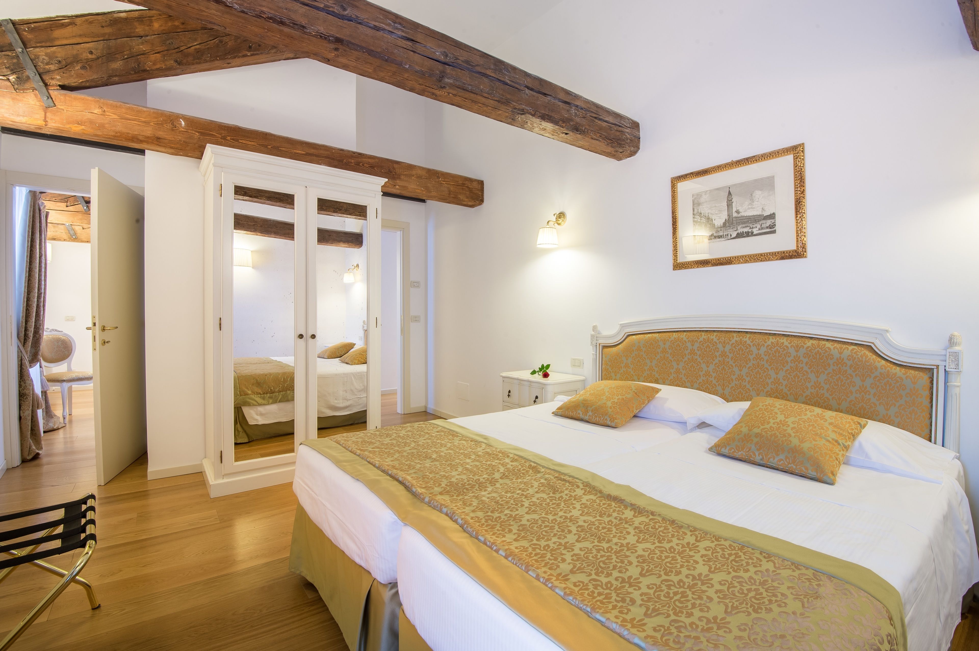 Un dormitorio con una cama grande, vigas de madera, un armario y un cuadro enmarcado en la pared.
