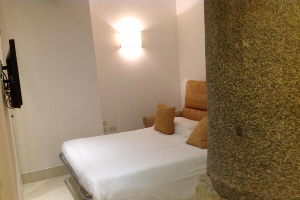 A bedroom with a bed, a nightstand, and a wall-mounted light fixture.