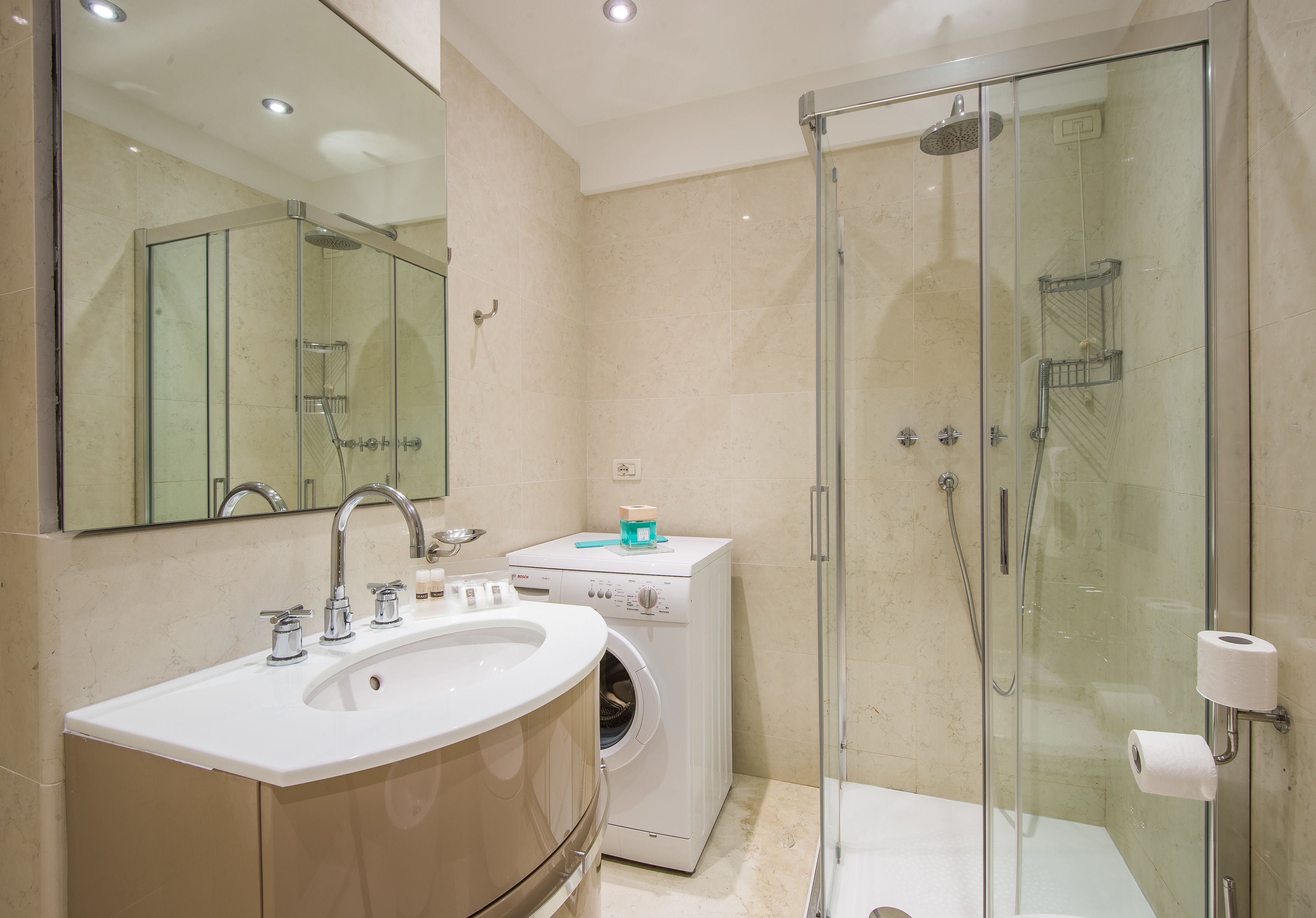 Une salle de bain moderne dotée d’une douche à parois de verre, d’un lave-linge encastré et d’un grand lavabo.