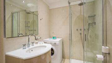 Une salle de bain moderne dotée d’une douche à parois de verre, d’un lave-linge encastré et d’un grand lavabo.