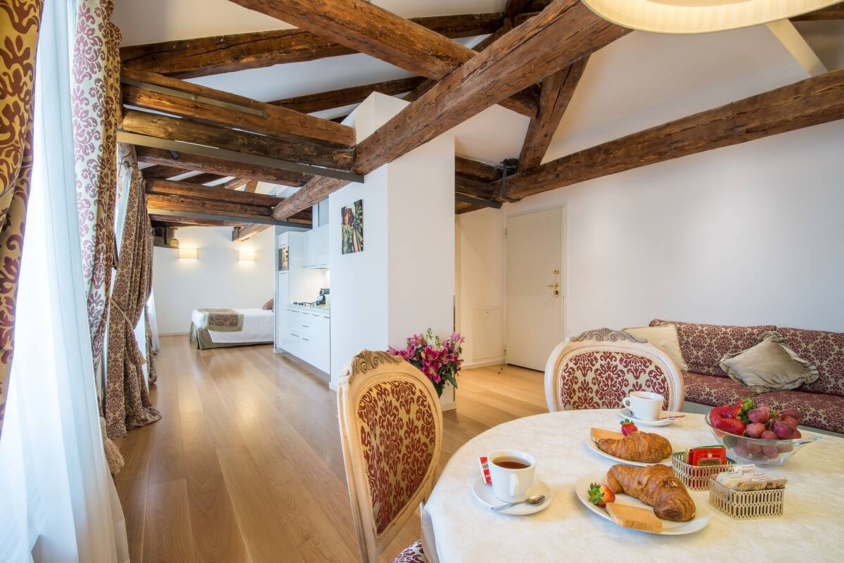 Ein gemütliches Zimmer mit Holzbalken, einem Esstisch mit Frühstück, einer Couch und einem Bett.