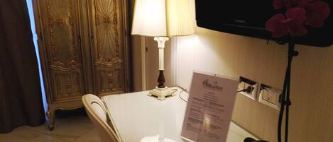 Ett hotellrum med ett vitt bord, en lampa, en tv och en blomsteruppsättning.