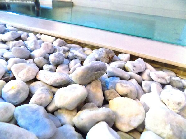 A close-up of smooth, rounded stones in a variety of shades of gray and white, arranged in a line beside a glass window. - Villa Del Mare (Rimini)