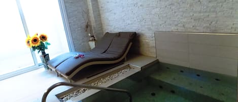 A spa room with a massage table, a small window with a view, a wall-mounted decoration, and a tiled floor.