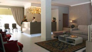 A modern living room with a reception desk, red chairs, a white sofa, and a patterned rug. - Hotel Douro Inn (Tabuaço)
