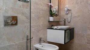 A modern bathroom with a glass-enclosed shower, a white toilet, a bidet, and a vanity with a mirror and a small potted plant.