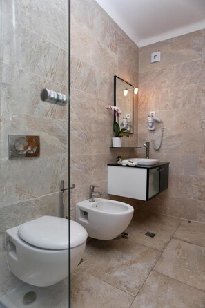 A modern bathroom with a glass-enclosed shower, a white toilet, a bidet, and a vanity with a mirror and a small potted plant.