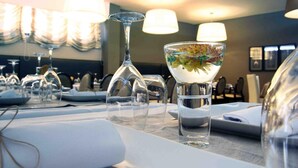 A dining table set with clear glassware, including wine glasses and a martini glass, in a well-lit room with modern decor. - Hotel Douro Inn (Tabuaço)