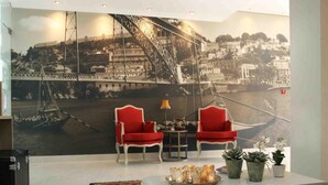 A living room with a large mural of a bridge, two red chairs, a small table with a lamp, and a tray of candles. - Hotel Douro Inn (Tabuaço)