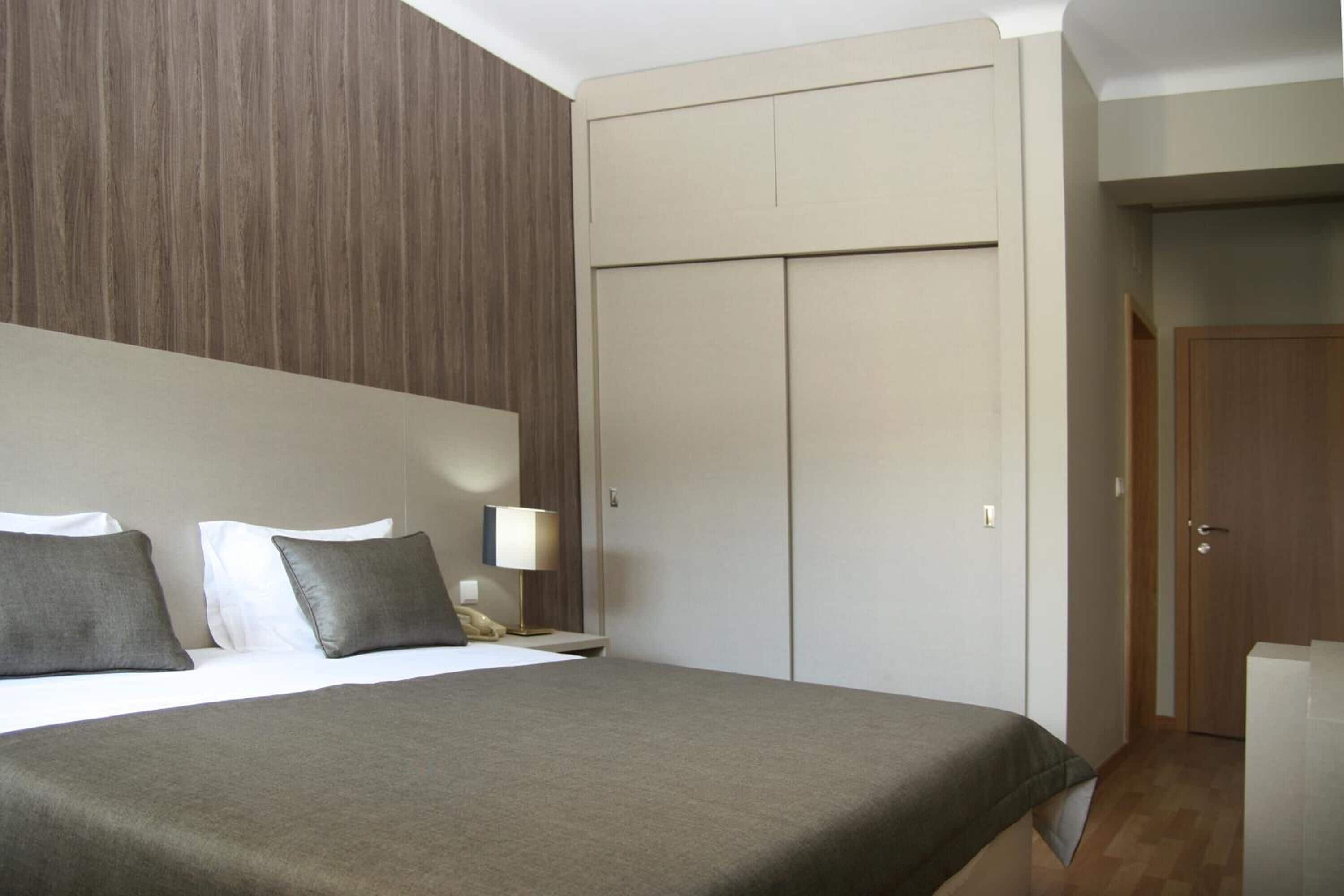 A hotel room with a bed, a nightstand, a lamp, and a wardrobe.