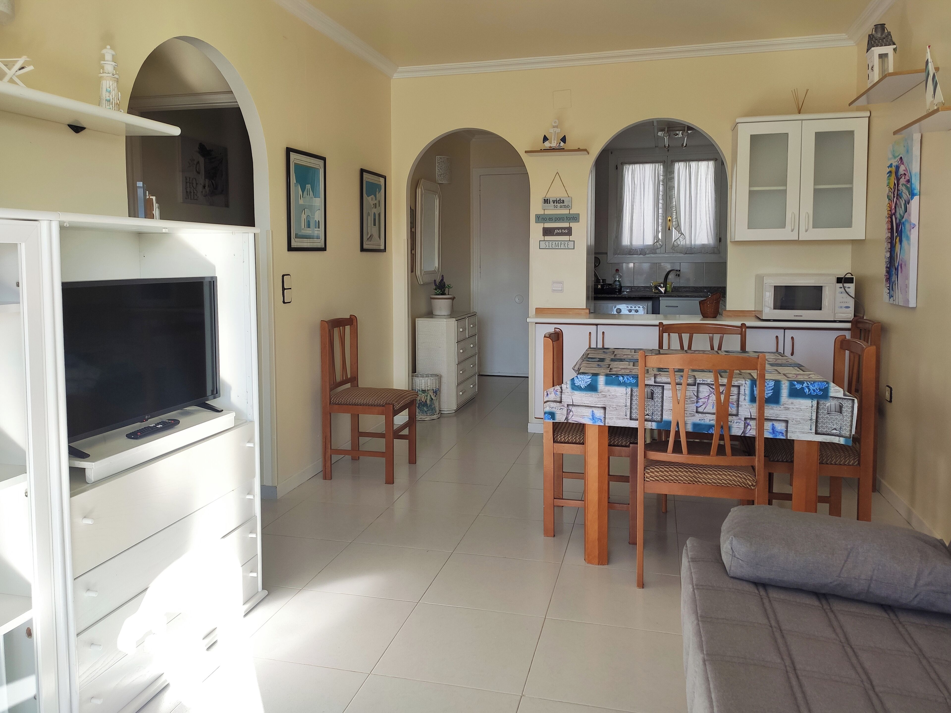 A living room with a TV, a sofa, a dining table with chairs, and a kitchen area with cabinets and a microwave.
