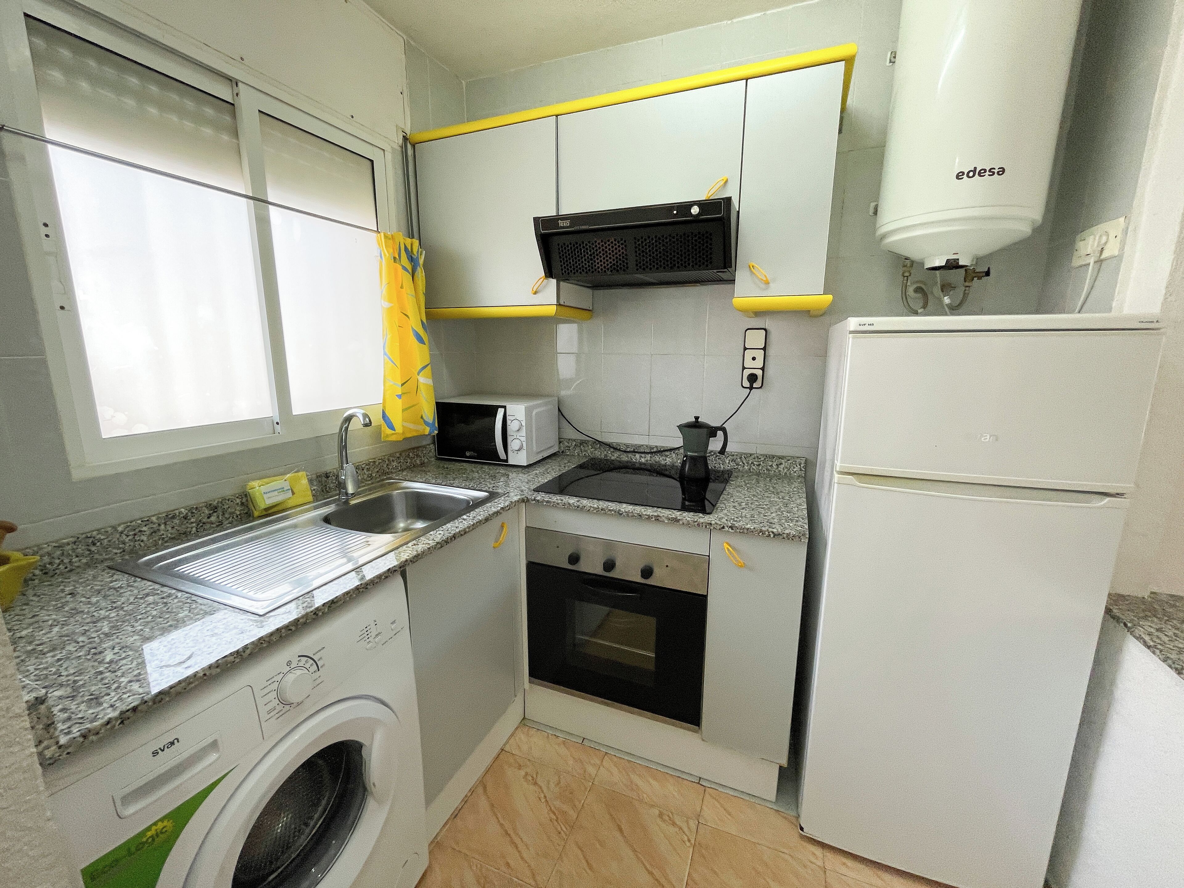 Cocina compacta equipada con lavadora, microondas, cocina y refrigerador.