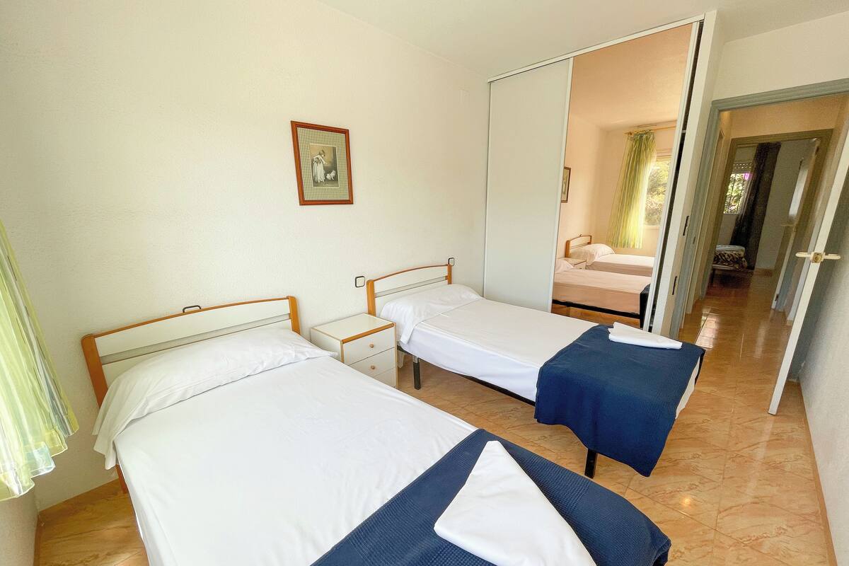 Habitación de hotel con dos camas individuales, una mesita de noche pequeña, un espejo y un cuadro en la pared.