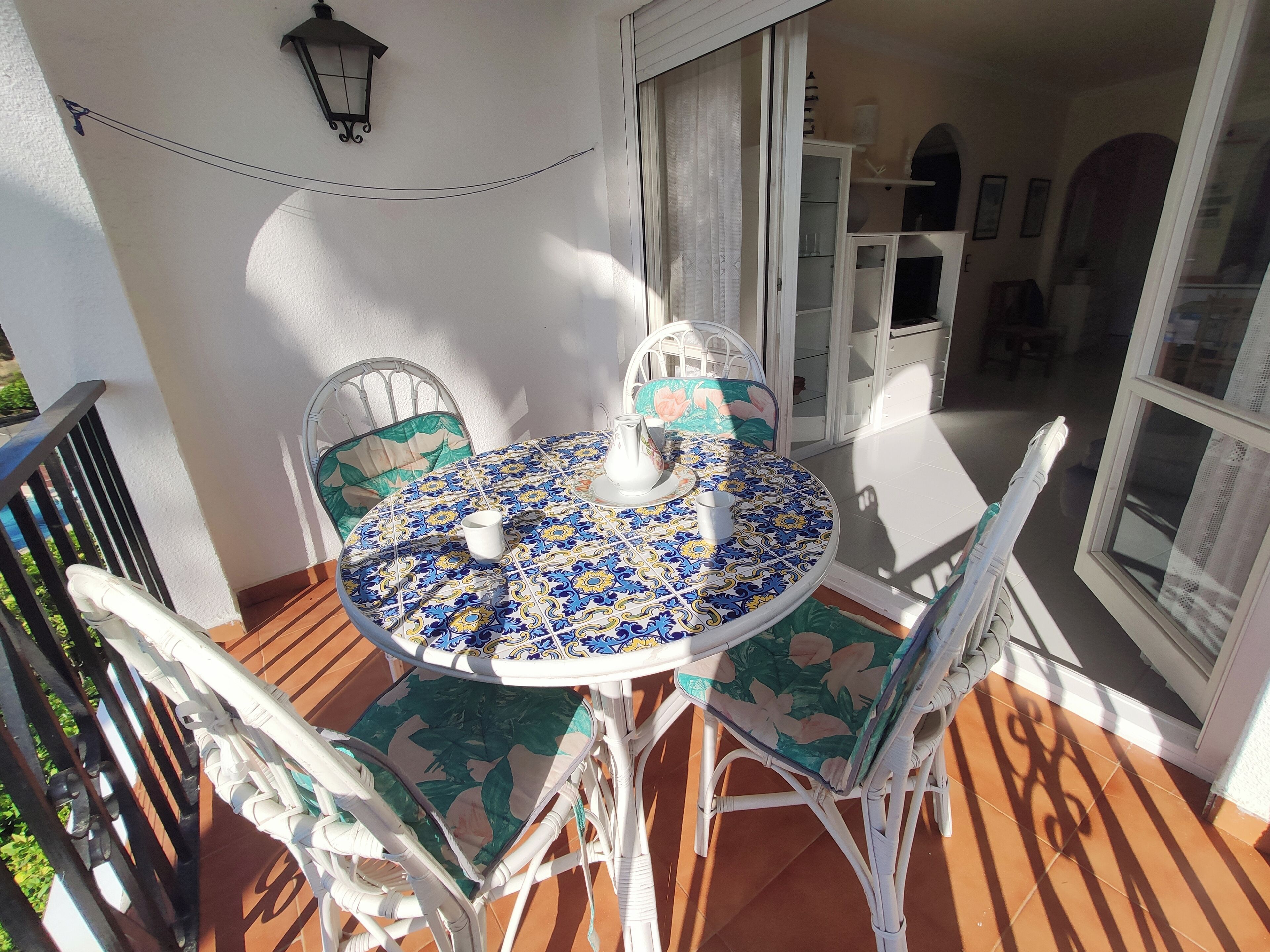 A round table with chairs on a balcony, a white cabinet, and a view of the interior.