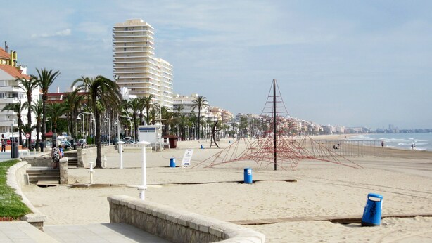 Uma praia com um edifício alto, palmeiras e um calçadão de areia.