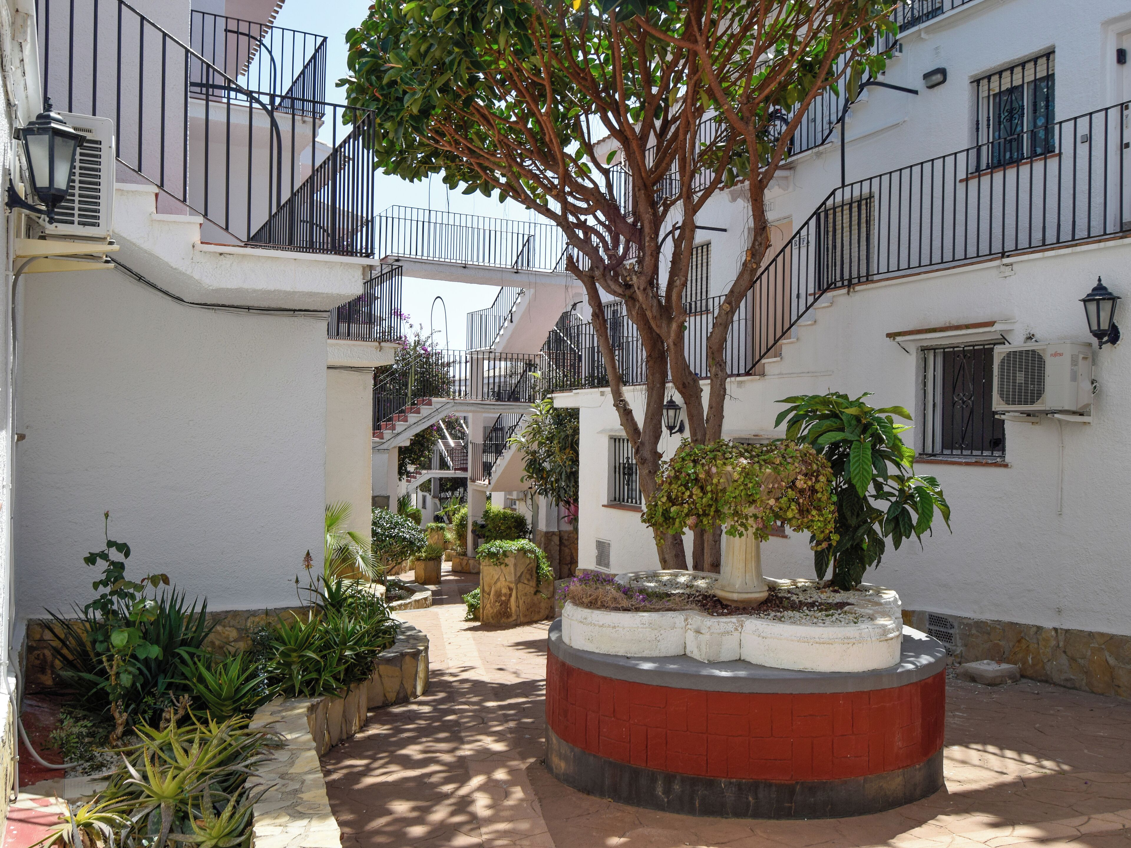 Une cour intérieure avec un jardin central, des bâtiments environnants dotés de balcons et un escalier.