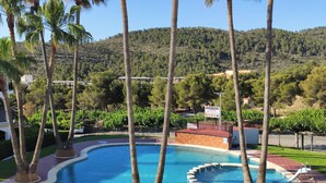 Uma piscina privativa com uma fonte de água azul cristalina, rodeada por palmeiras e uma paisagem montanhosa ao fundo.