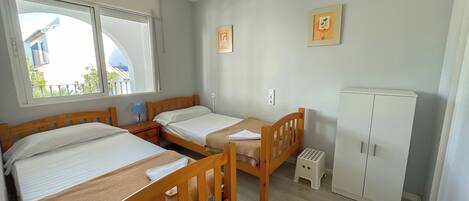 Ein Zimmer mit zwei Holzbett, einem Deckenventilator, einem weißen Kleiderschrank und einem Fenster mit Blick auf Gebäude.