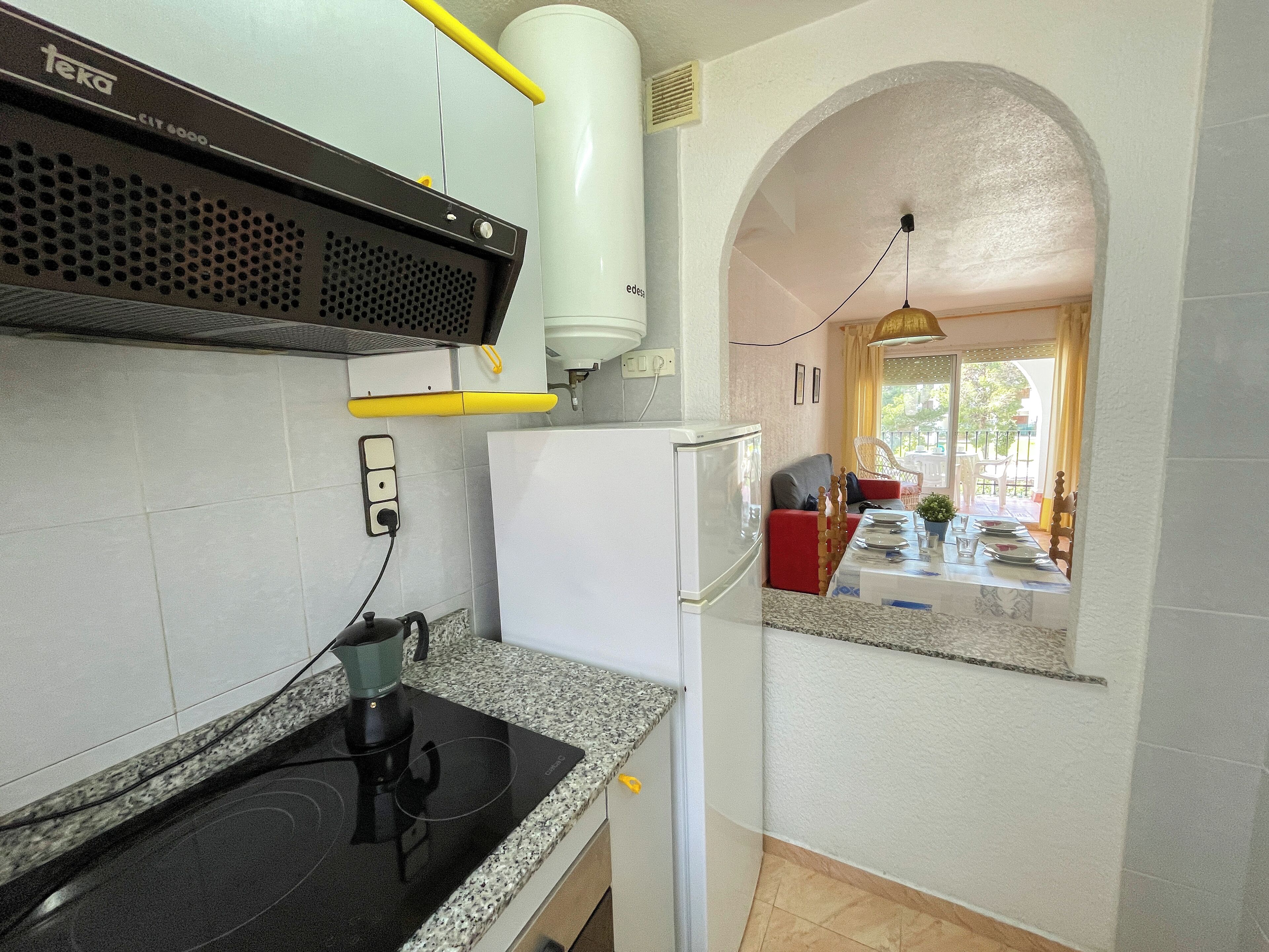 A kitchen with a stove, refrigerator, and a window overlooking a balcony.