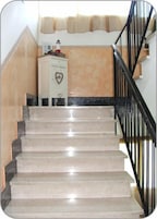 Una escalera de mármol con un adorno con forma de corazón en un mueble, que lleva a una habitación con pared color beige y barandilla negra.