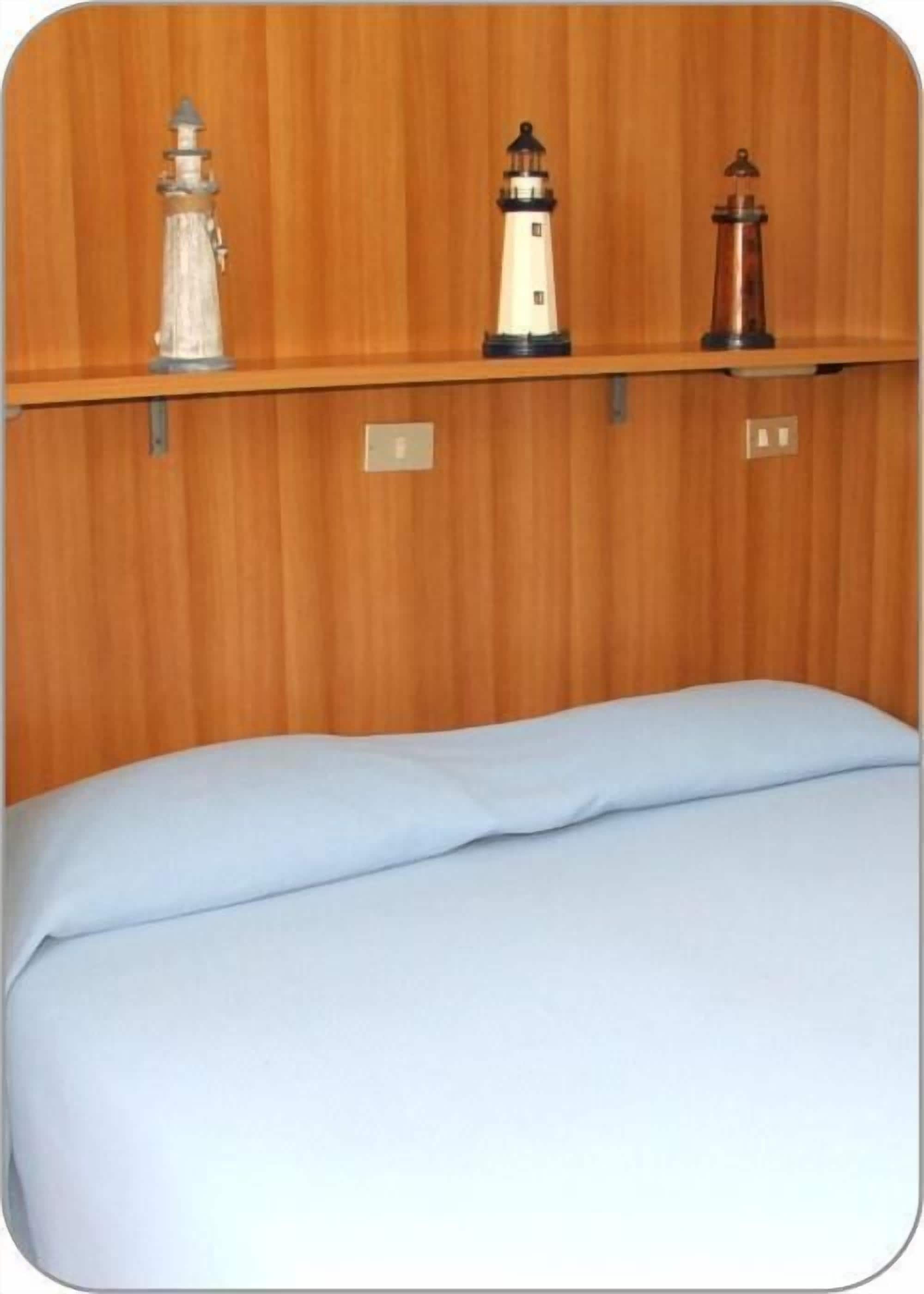 Una habitación con pared de madera, una cama con sábana blanca y tres faros en un estante.