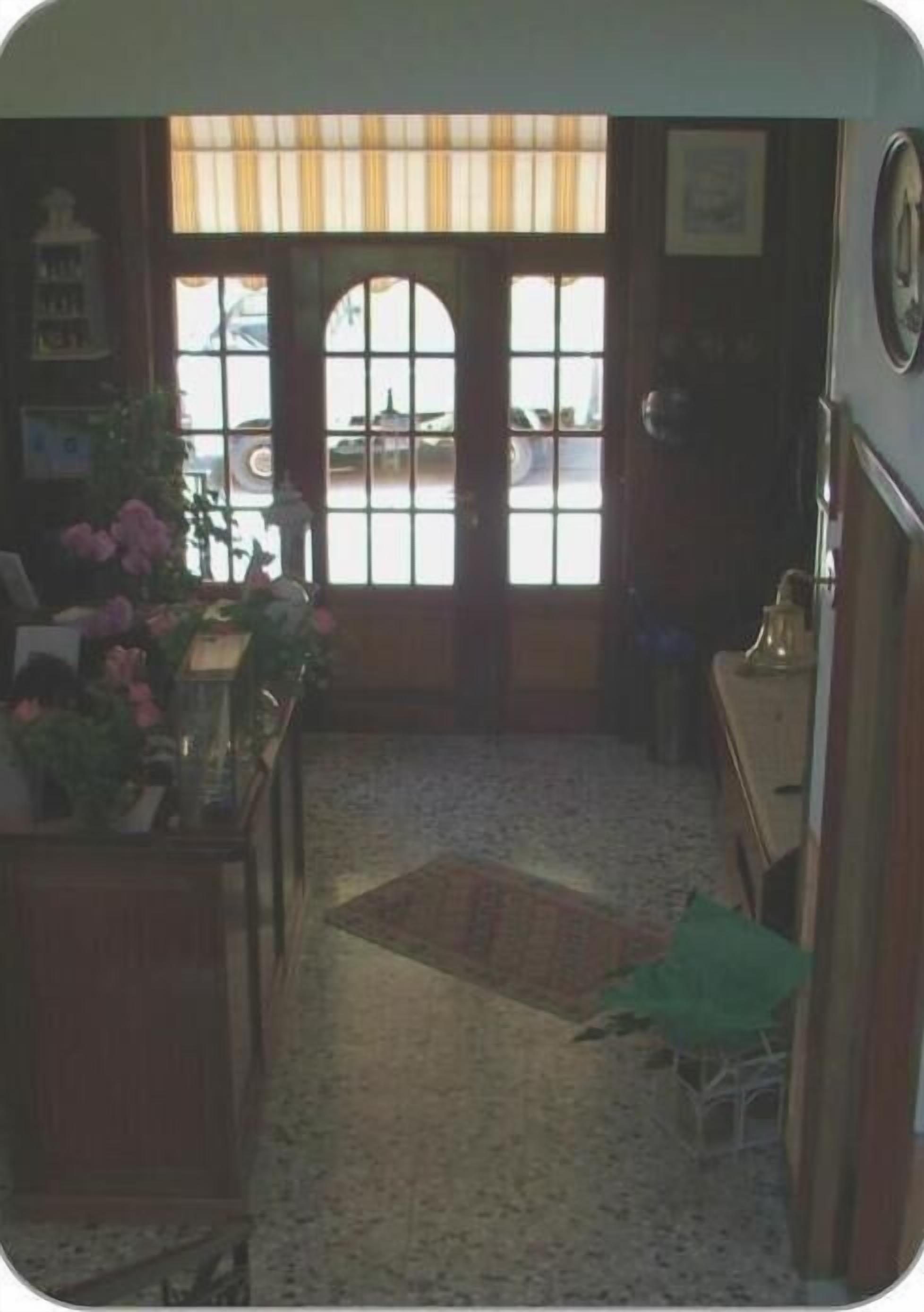 A room with a wooden floor, a green plant, a table with flowers, and a window with curtains.