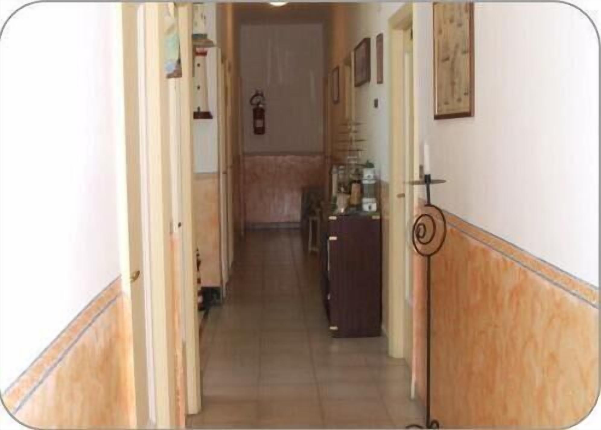 Un pasillo estrecho con suelo de madera, una puerta a la izquierda y un extintor fijo en la pared.