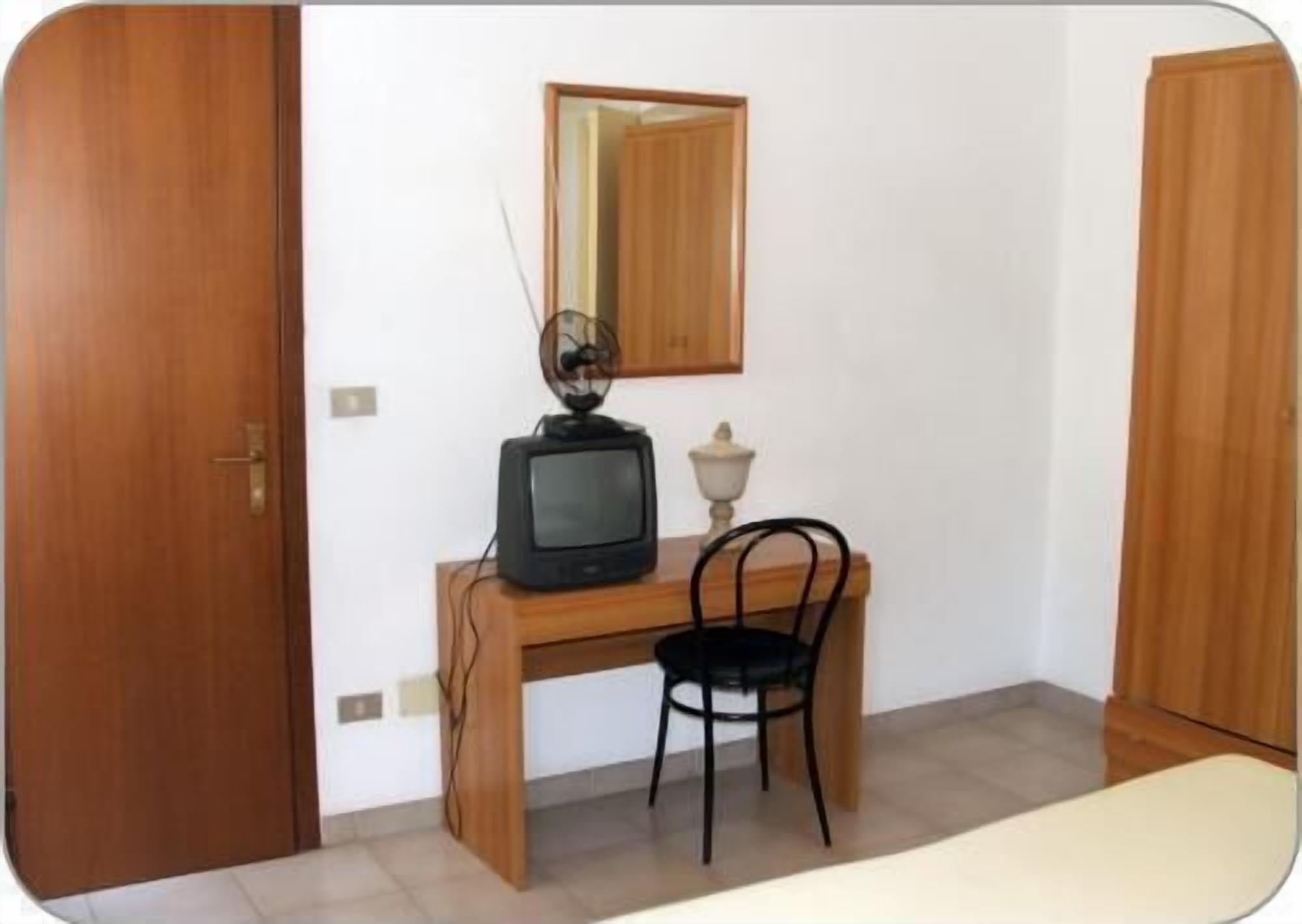 A small room with a wooden desk, a television, a chair, and a mirror on the wall.