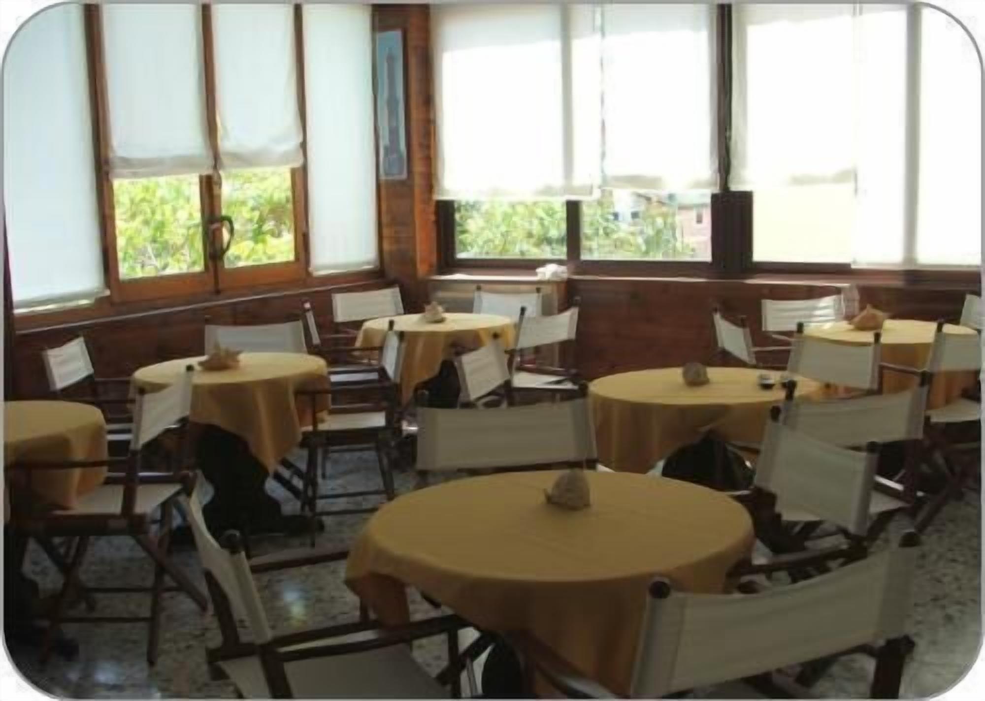 Un espace repas avec des tables et des chaises rondes, de grandes fenêtres équipées de stores et une vue sur la verdure environnante.