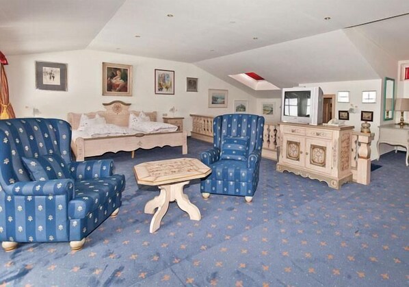 A room with a bed, two blue armchairs, a small table, and a TV on a stand. - Hahnenhof (Kitzbuehel)