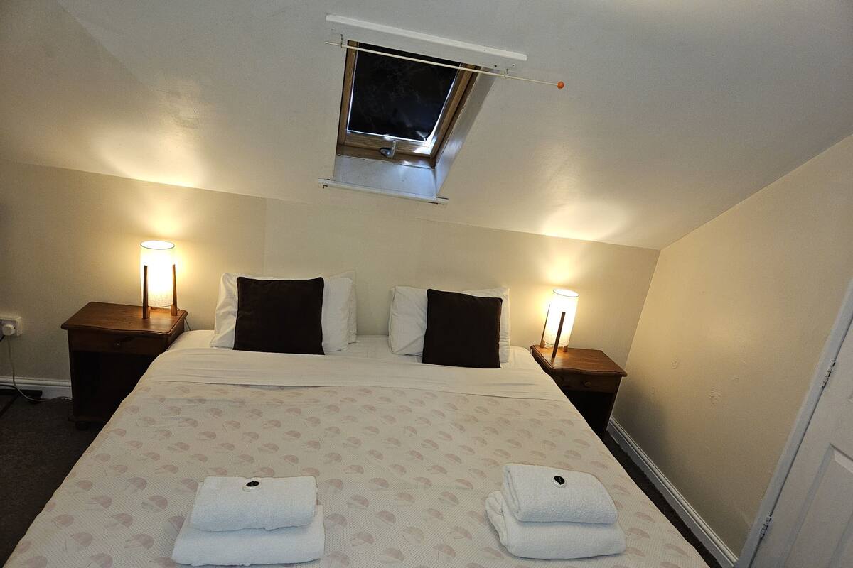 A hotel room with a large bed, two bedside tables with lamps, a window, and a door.