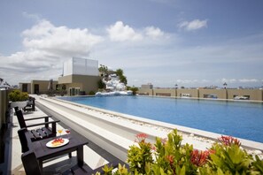 A rooftop pool with a waterfall feature, lounge chairs, and a dining table with a plate of food.