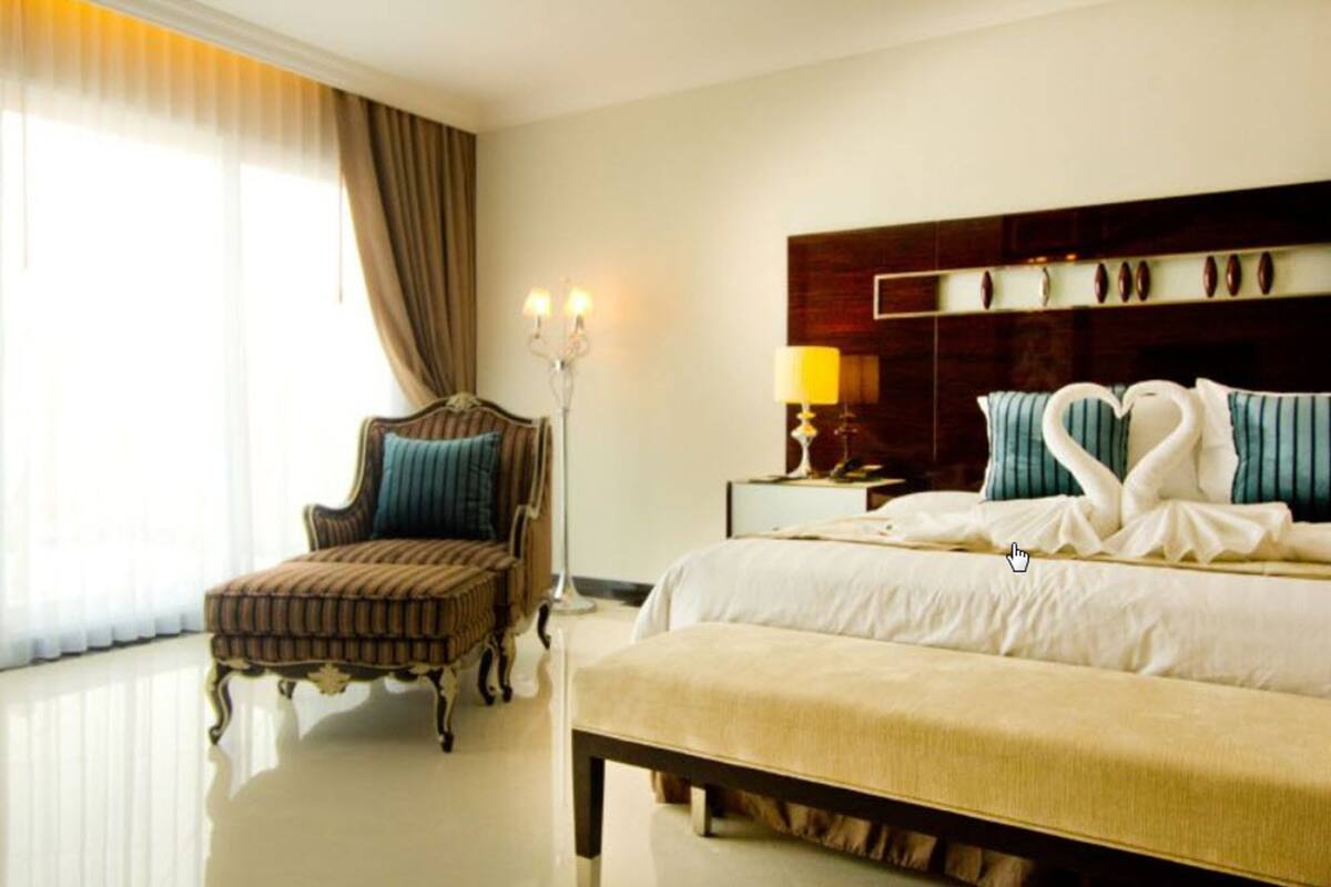 A hotel room with a large bed, a chair, a nightstand with a lamp, and a window with curtains.