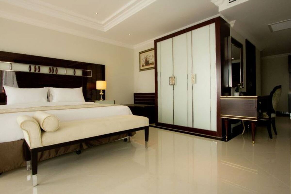 A hotel room with a large bed, a bedside table with a lamp, a wardrobe, and a mirror.