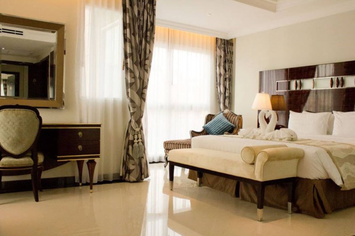 A hotel room with a large bed, a bedside table, a chair, a mirror, and curtains.