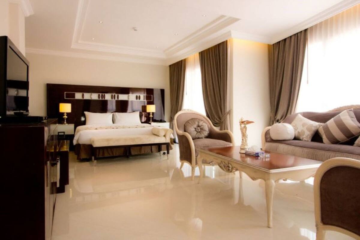 A hotel room with a bed, a sofa, a dining table, and a TV.