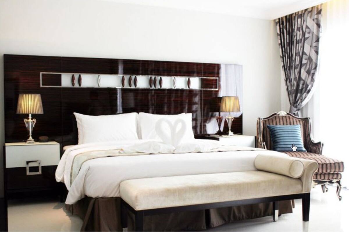 A modern hotel room with a large bed, two bedside tables with lamps, a bench, and a patterned curtain.