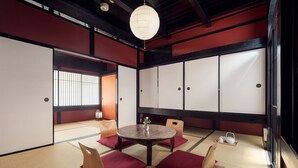 A traditional Japanese room with tatami flooring, a round table with cushions, sliding doors, and a hanging light fixture.