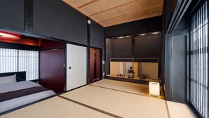 A traditional Japanese-style room with tatami flooring, a bed, sliding doors, and a view of the outside through a window with vertical blinds.
