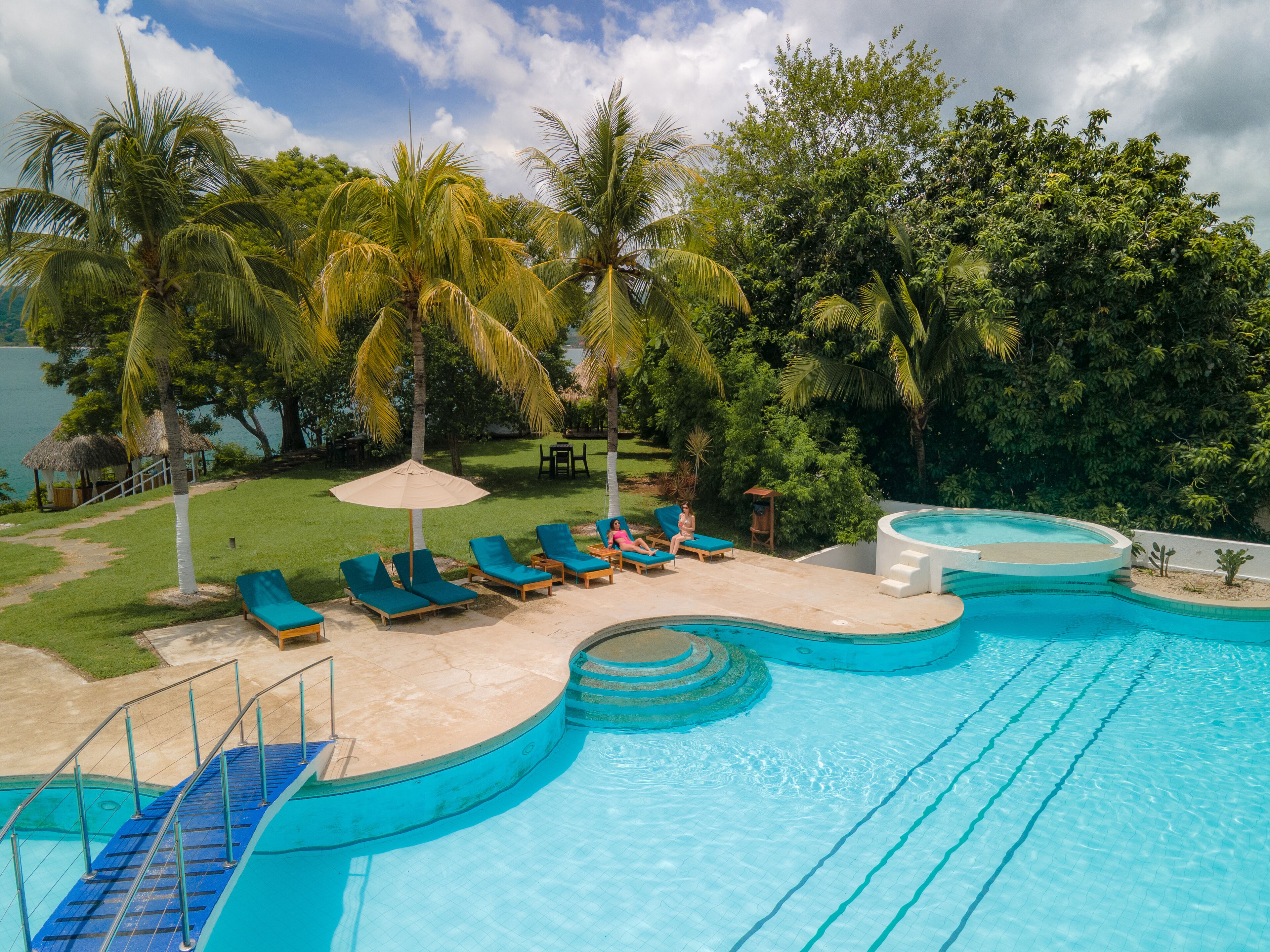 A swimming pool with blue water, surrounded by lounge chairs and palm trees.