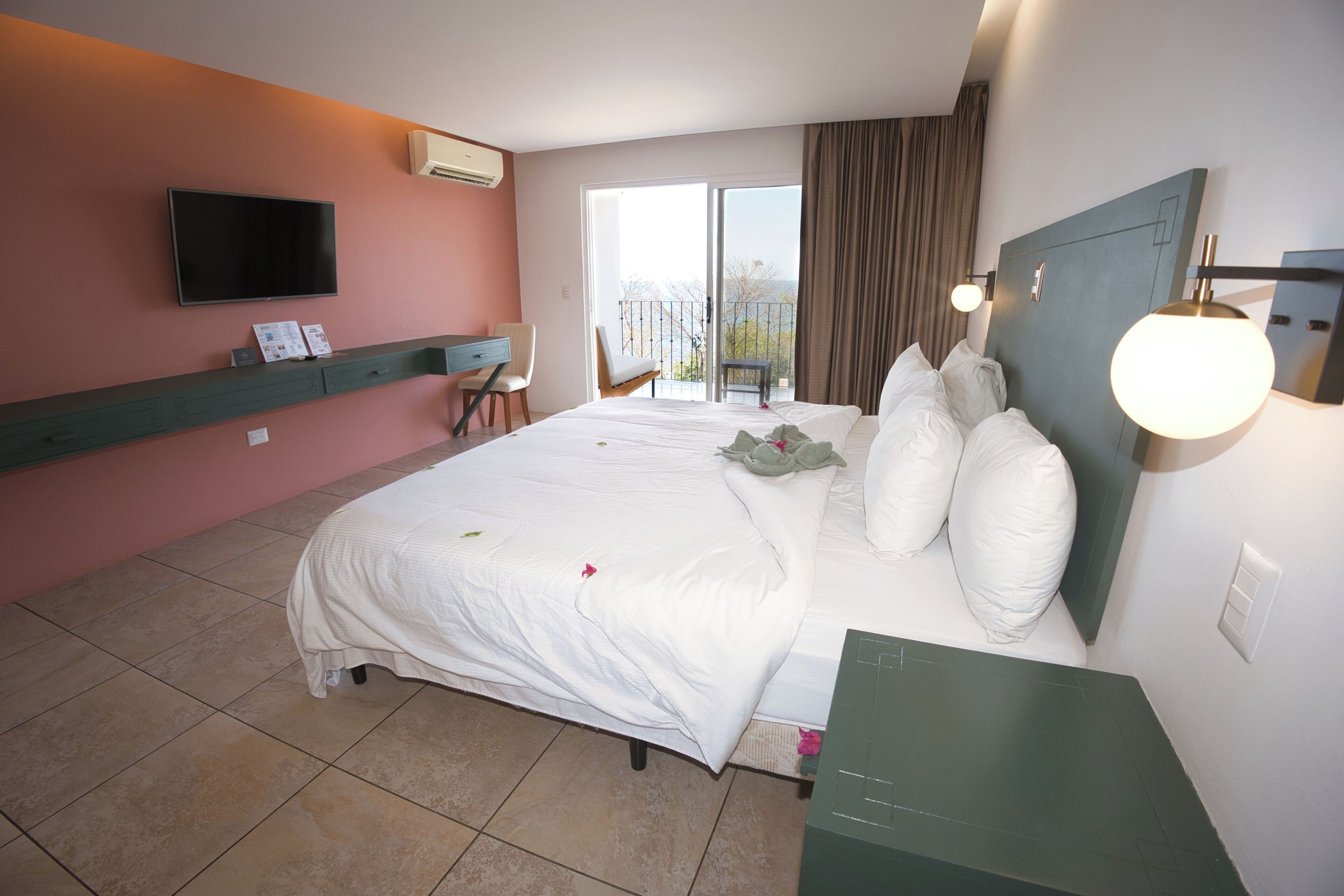 A hotel room with a bed, a TV mounted on the wall, a desk, and a chair.