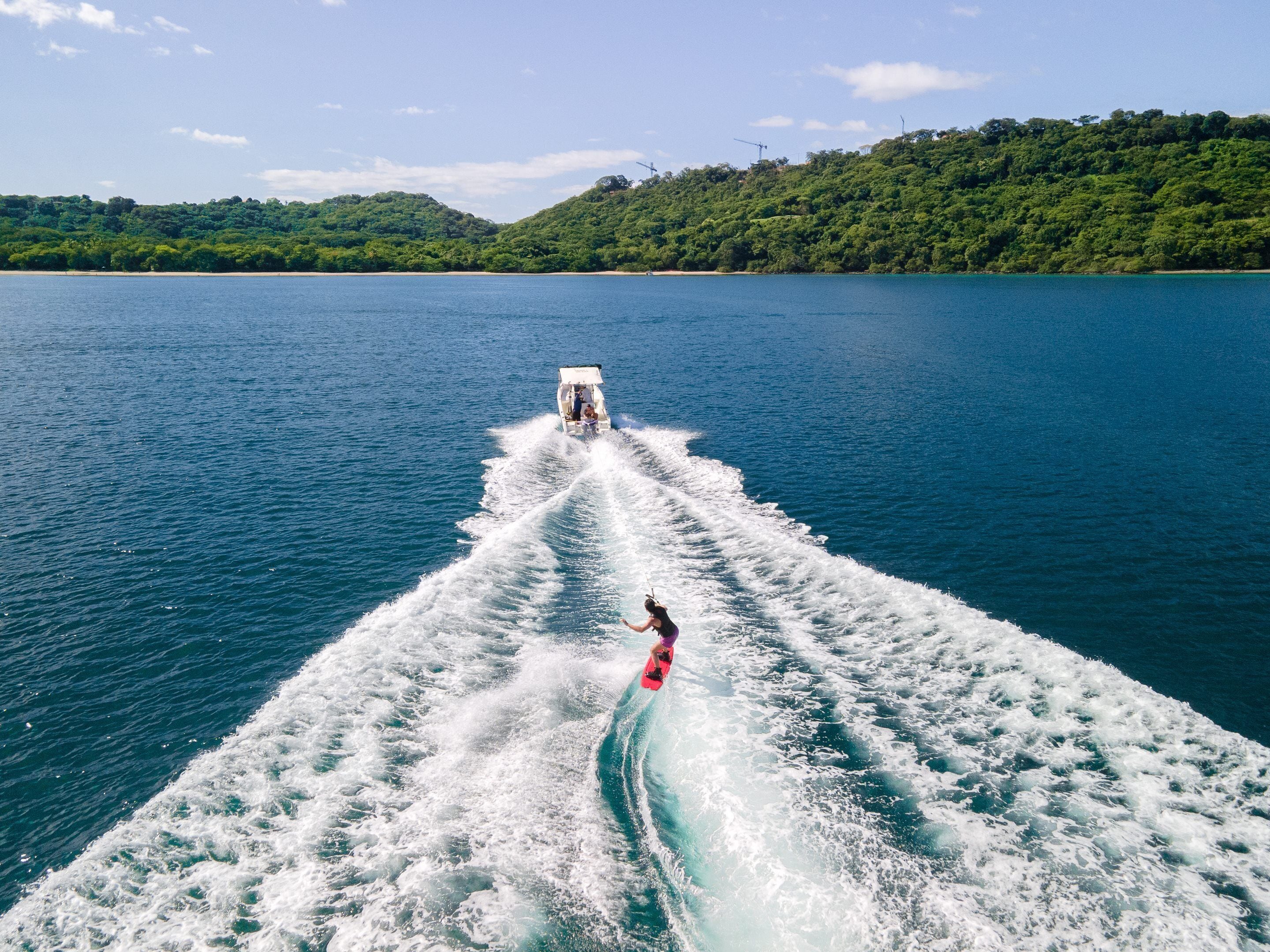 Un bote avanza a toda velocidad sobre un lago tranquilo, con una persona practicando wakeboard a su estela.