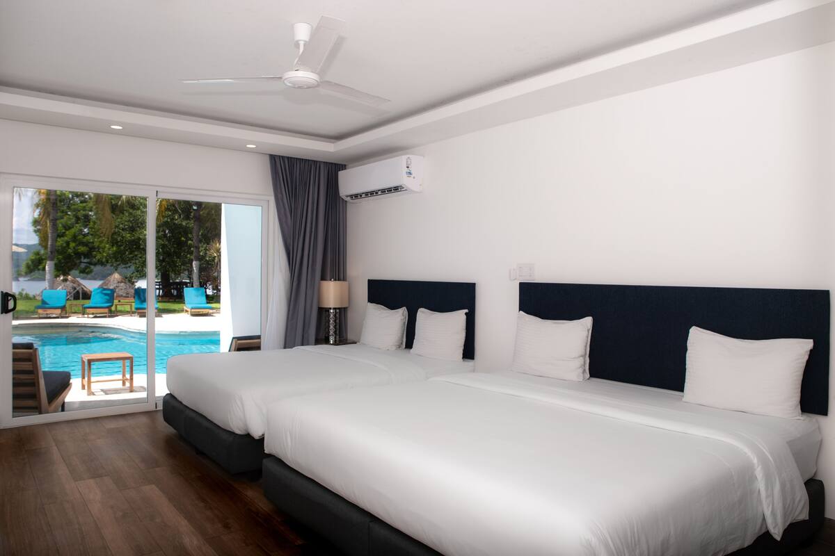 A hotel room with a large bed, a ceiling fan, an air conditioning unit, a view of a swimming pool, and a sliding glass door.
