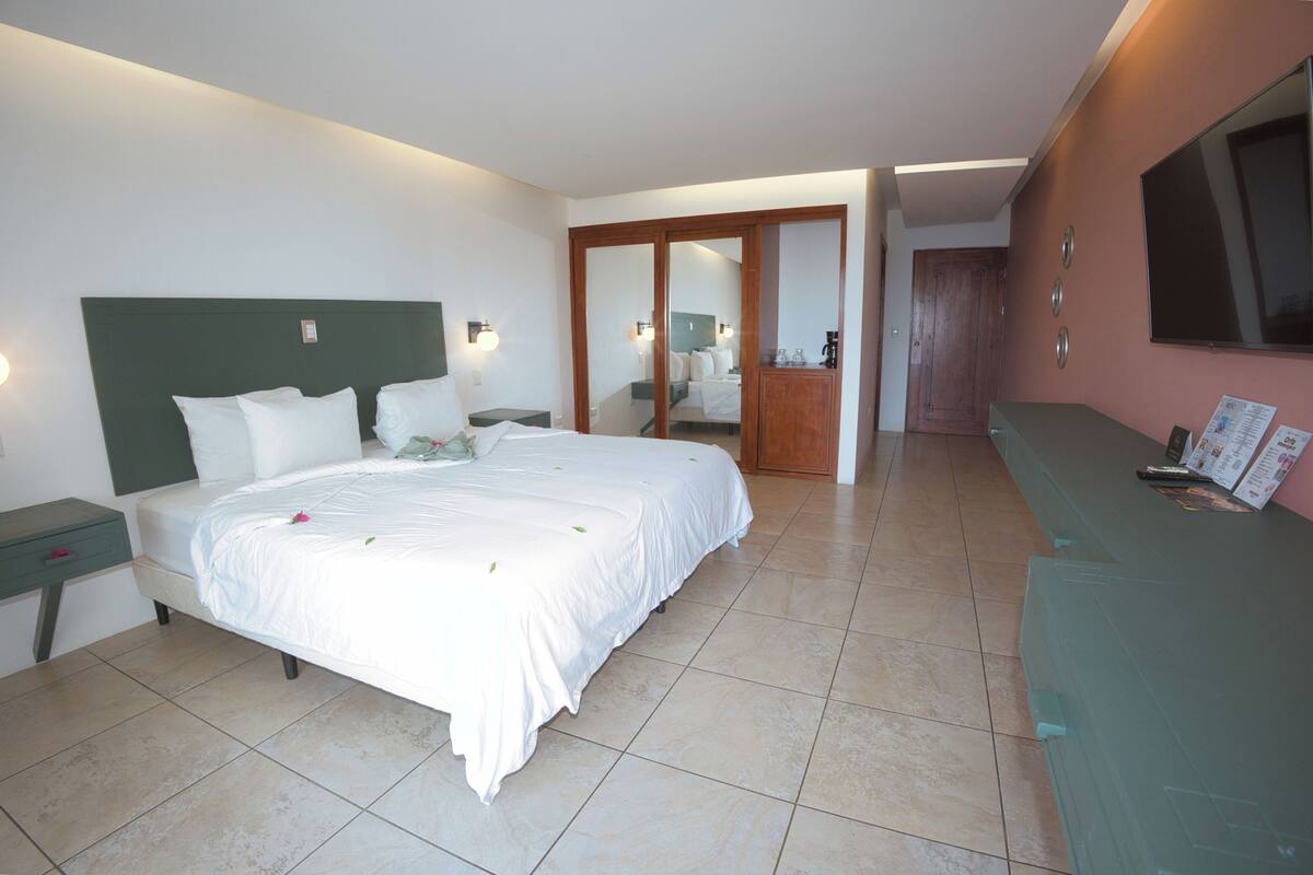 A hotel room with a large bed, a nightstand, a dresser, and a mirror.