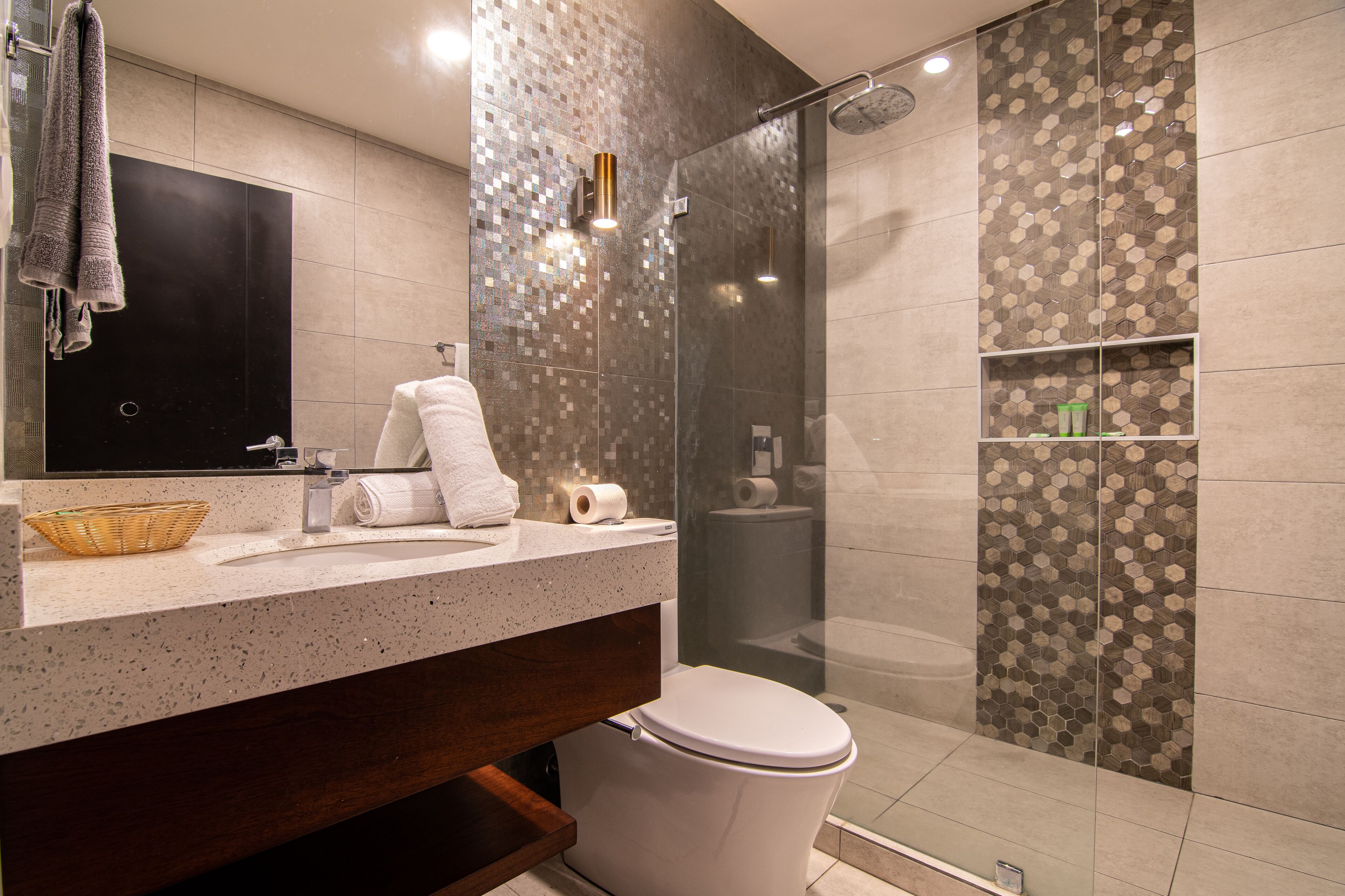 Un baño moderno con cabina de ducha de vidrio, lavabo con espejo e inodoro.