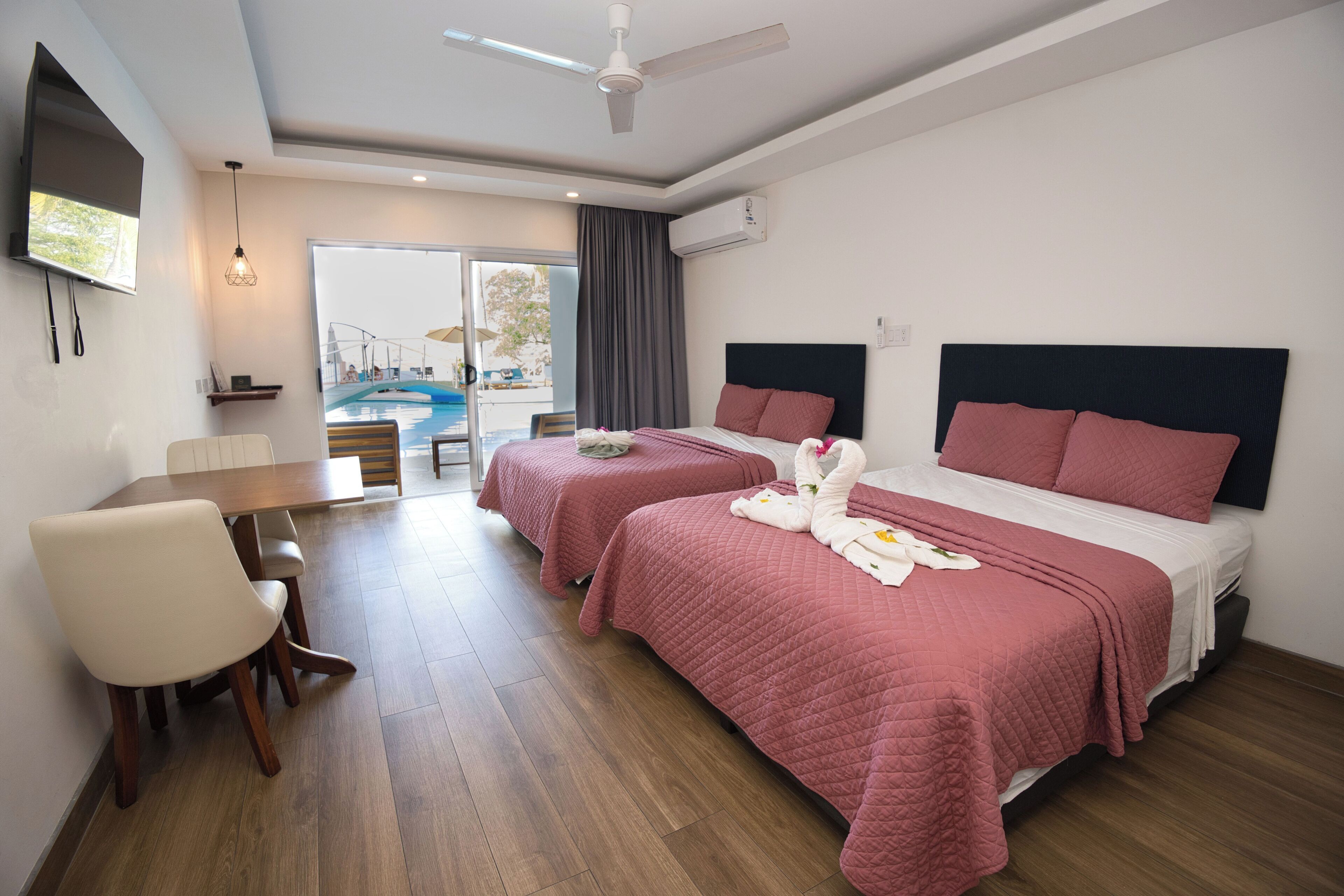 Une chambre d’hôtel avec deux lits, une table à manger, un téléviseur et un ventilateur de plafond.